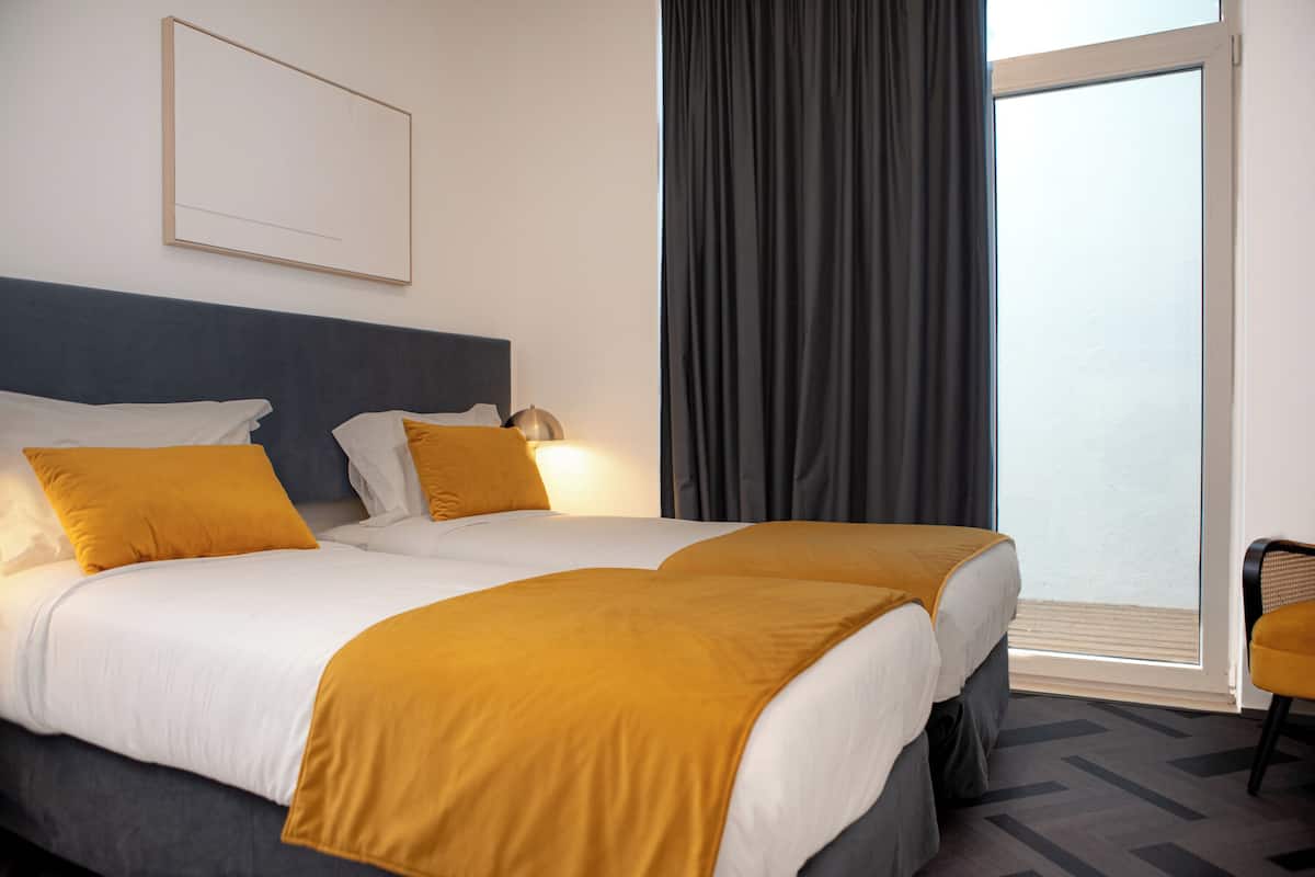 A hotel room with two beds, a large window with curtains, and a chair.
