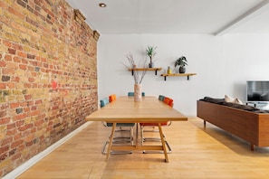 A dining area with a long wooden table, chairs, a brick wall, and a TV on the right. - Central Urban Retreat in Shoreditch - Old Street (London)