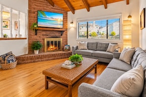 A cozy living room with a fireplace, a large TV, and a comfortable sofa. - 25% Off Oct 22-25 Walk 2 Beach, Rooftop Deck View! (Oxnard)