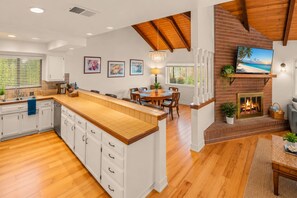 Uma cozinha ampla com uma ilha grande, piso de madeira e lareira de tijolos.