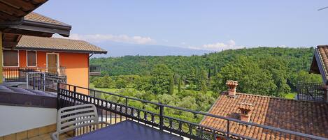 A balcony with a table and chairs, overlooking a lush green landscape and distant mountains.