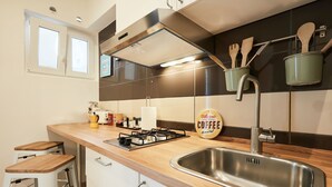 Une cuisine moderne dotée d’un évier en acier inoxydable, de tabourets en bois, d’une cuisinière à gaz et d’ustensiles suspendus.