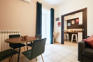 Un soggiorno moderno con zona pranzo, che include un tavolo rotondo, sedie verde scuro e un divano con un cuscino rosso.