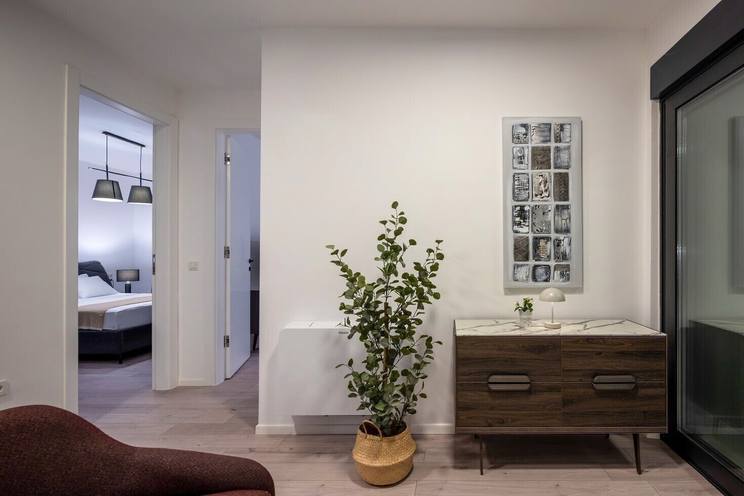 Una habitación de hotel moderna con cama, mesita de noche, lámpara y un ventanal grande.