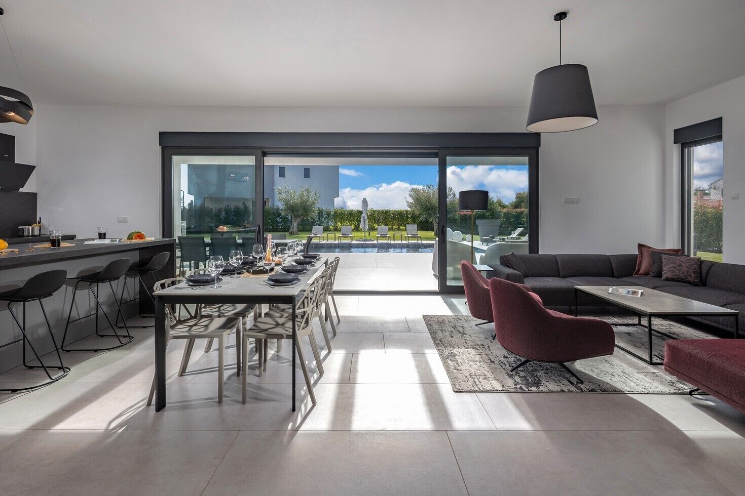 A modern kitchen with a dining area, large sliding glass doors leading to a pool, and a seating area with a sofa and chairs.