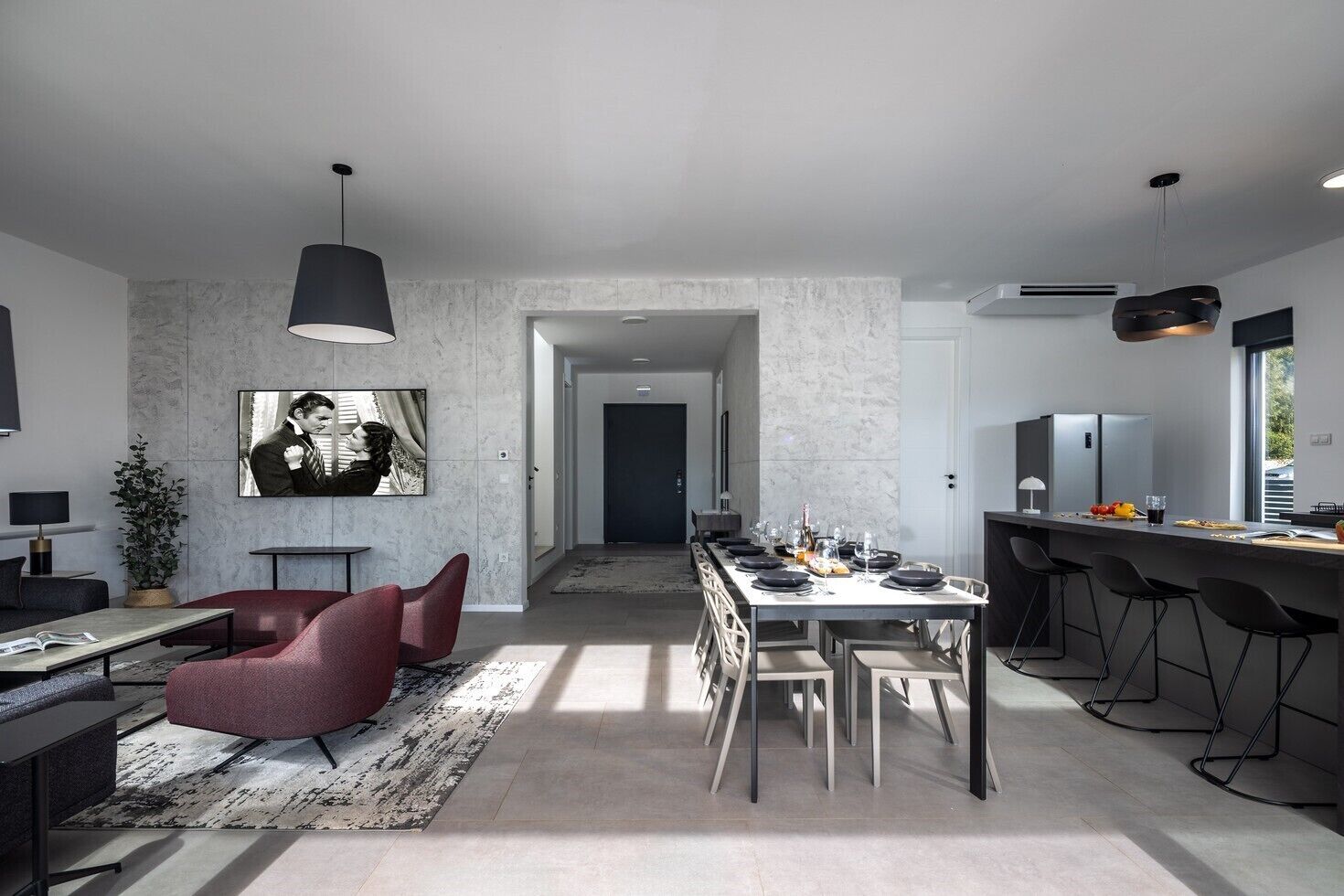 A modern kitchen with a long dining table, bar stools, and a large window.