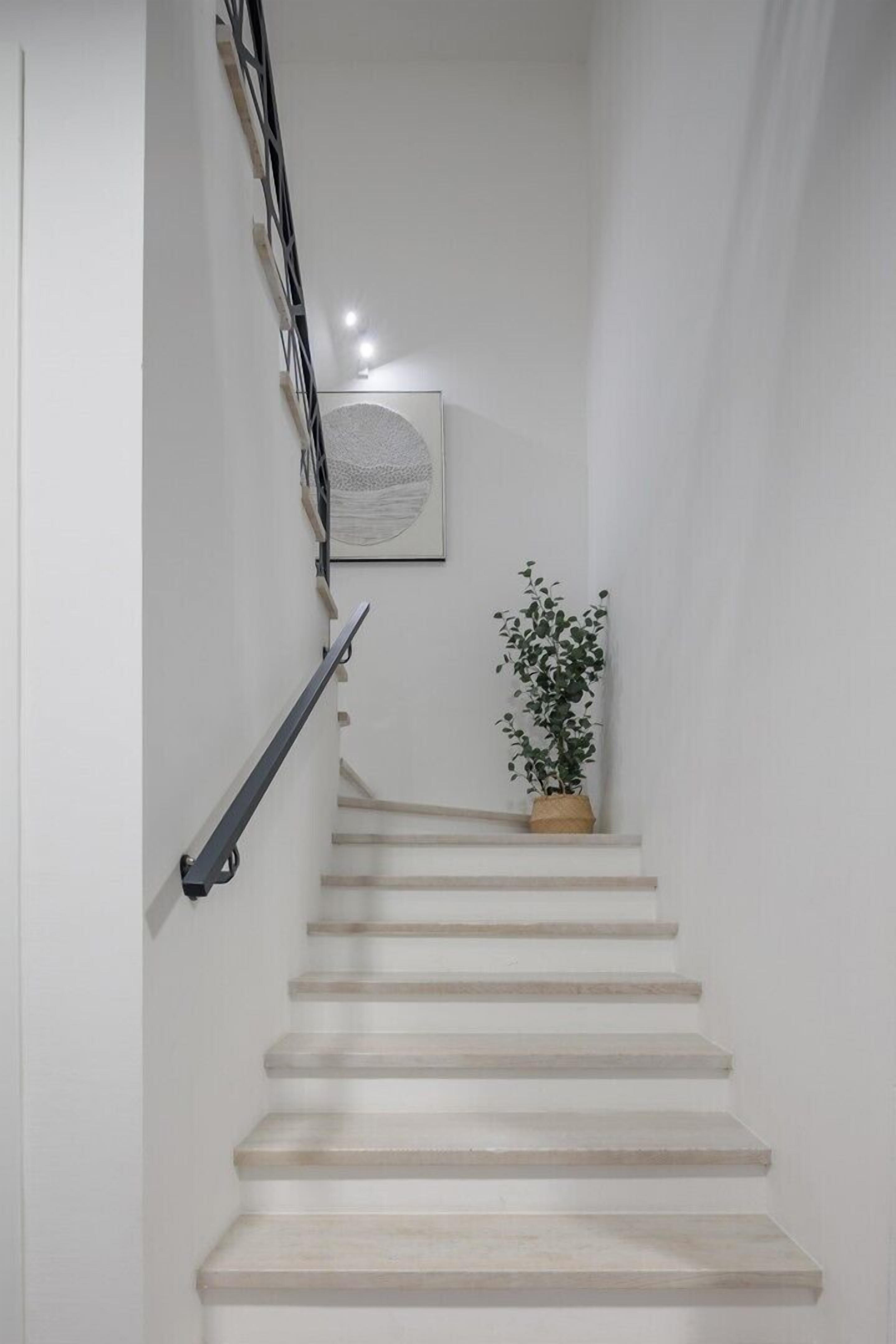Una escalera con barandilla, una planta en maceta y un cuadro colgado en la pared.