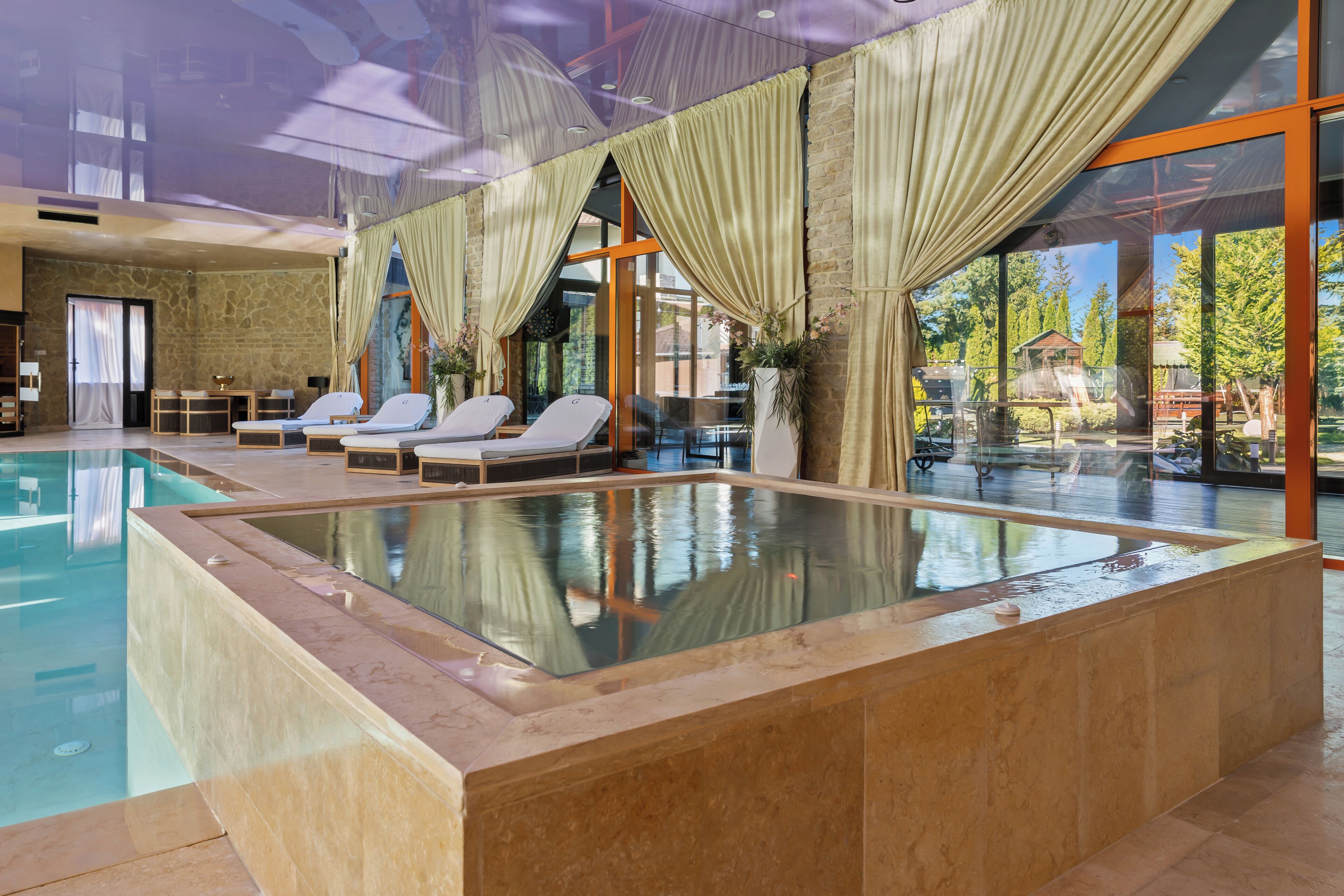 Ein moderner, überdachter Pool mit klarem Wasser, umgeben von Liegestühlen und großen Fenstern.