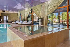 Ein moderner, überdachter Pool mit klarem Wasser, umgeben von Liegestühlen und großen Fenstern.