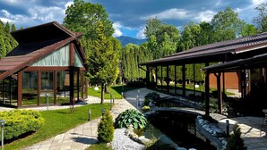 A modern building with large glass windows, a covered outdoor area, and a small pond.