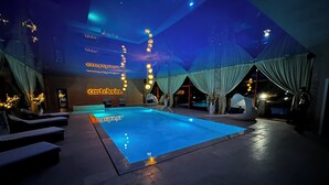 An indoor swimming pool with lounge chairs and a ceiling with hanging lights.