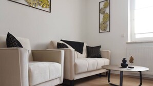 A modern living room with two beige sofas, a round coffee table, and decorative wall art. - Timber Suite - near Rußweiher (Eschenbach in der Oberpfalz)