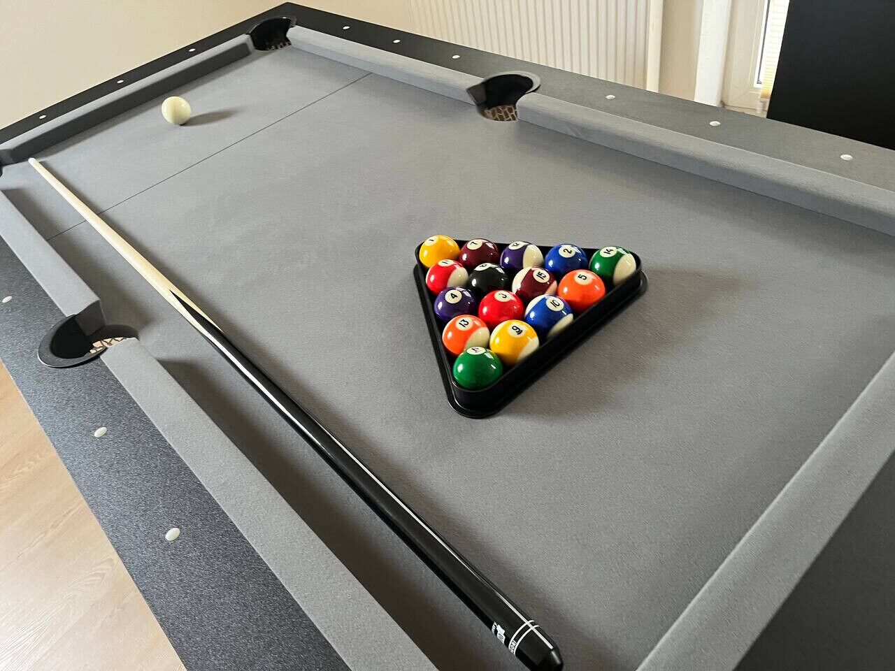 Una mesa de billar con un montón triangular de bolas de billar, una vara y una bola suelta sobre la mesa.