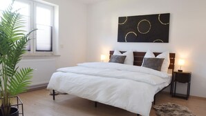 A bedroom with a bed, bedside tables, a potted plant, and a wall art piece. - Timber Suite - near Rußweiher (Eschenbach in der Oberpfalz)