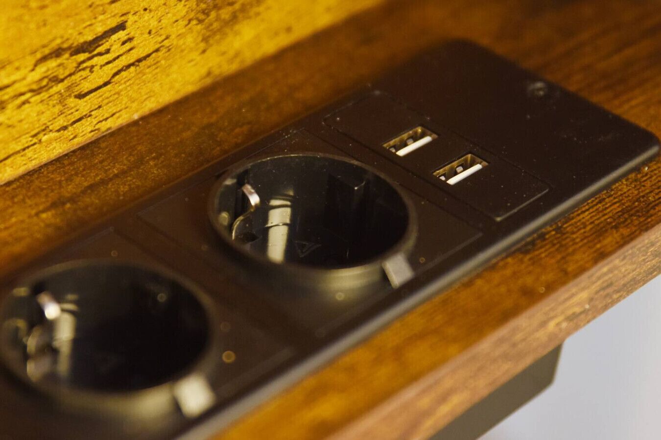 A black electrical outlet with two holes, likely for plugs, on a wooden surface.