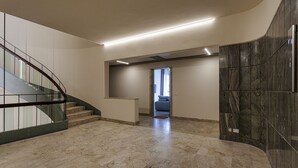 Een ruime lobby met een marmeren vloer, een gebogen trap en uitzicht op een slaapkamer.