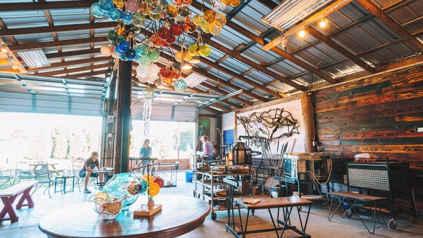 An interior with a rustic wooden wall, a hanging glass ornament, and a table with a vase of flowers.