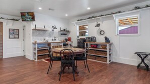 A dining area with a wooden table and chairs, a kitchen with white cabinets and a tiled backsplash, and a window with a purple curtain.