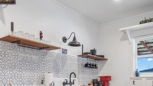 A compact kitchen with a tiled backsplash, a sink, and wooden shelves.