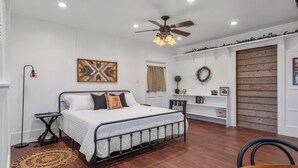 A bedroom with a bed, a ceiling fan, a shelf with books, and a door.