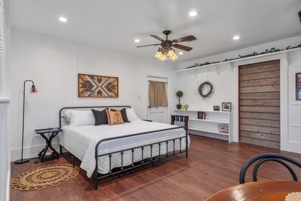 A bedroom with a bed, a ceiling fan, a shelf with books, and a door.