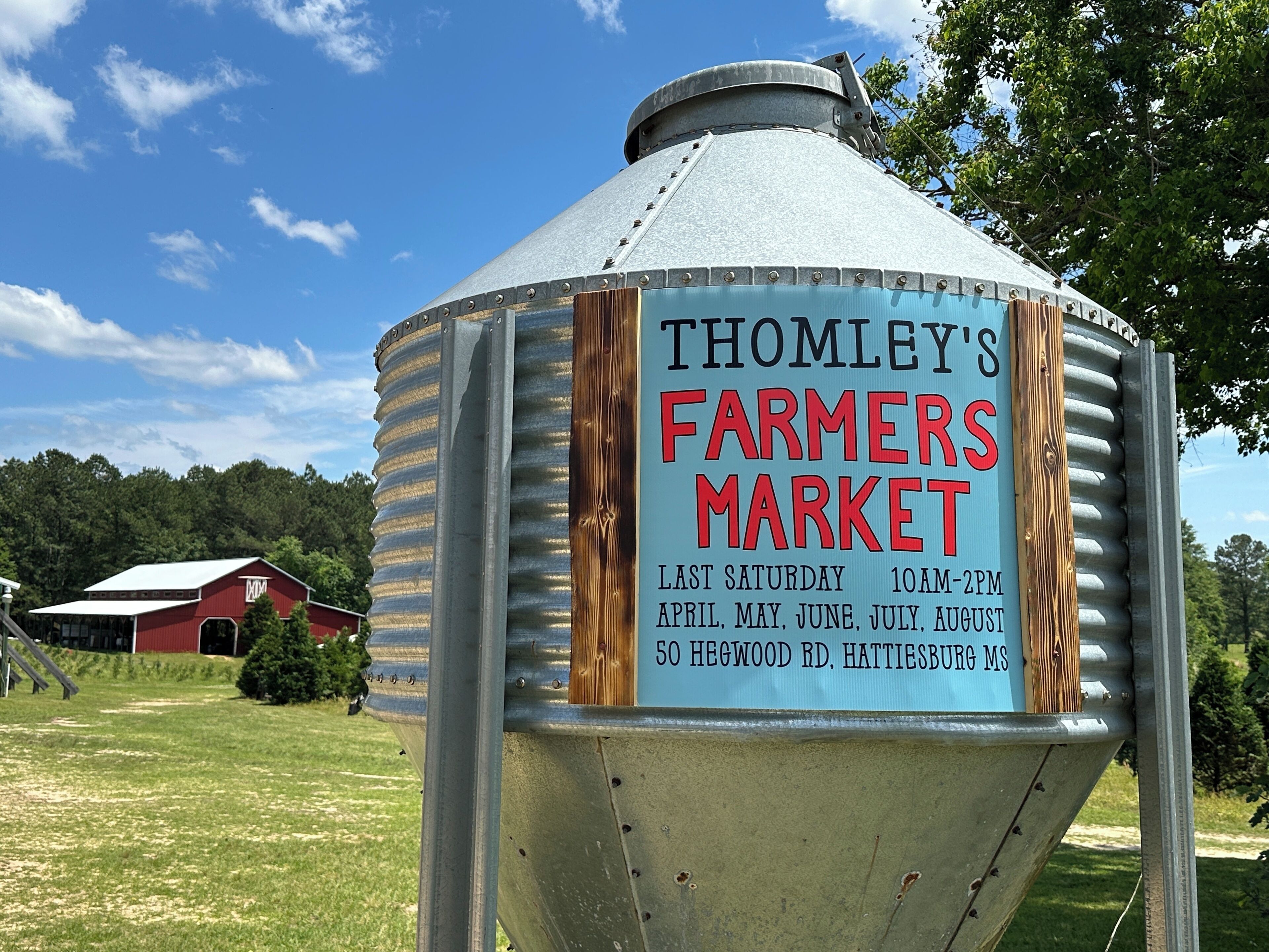 A metal structure with a sign for Thomley's Farmers Market, listing operating days and hours.