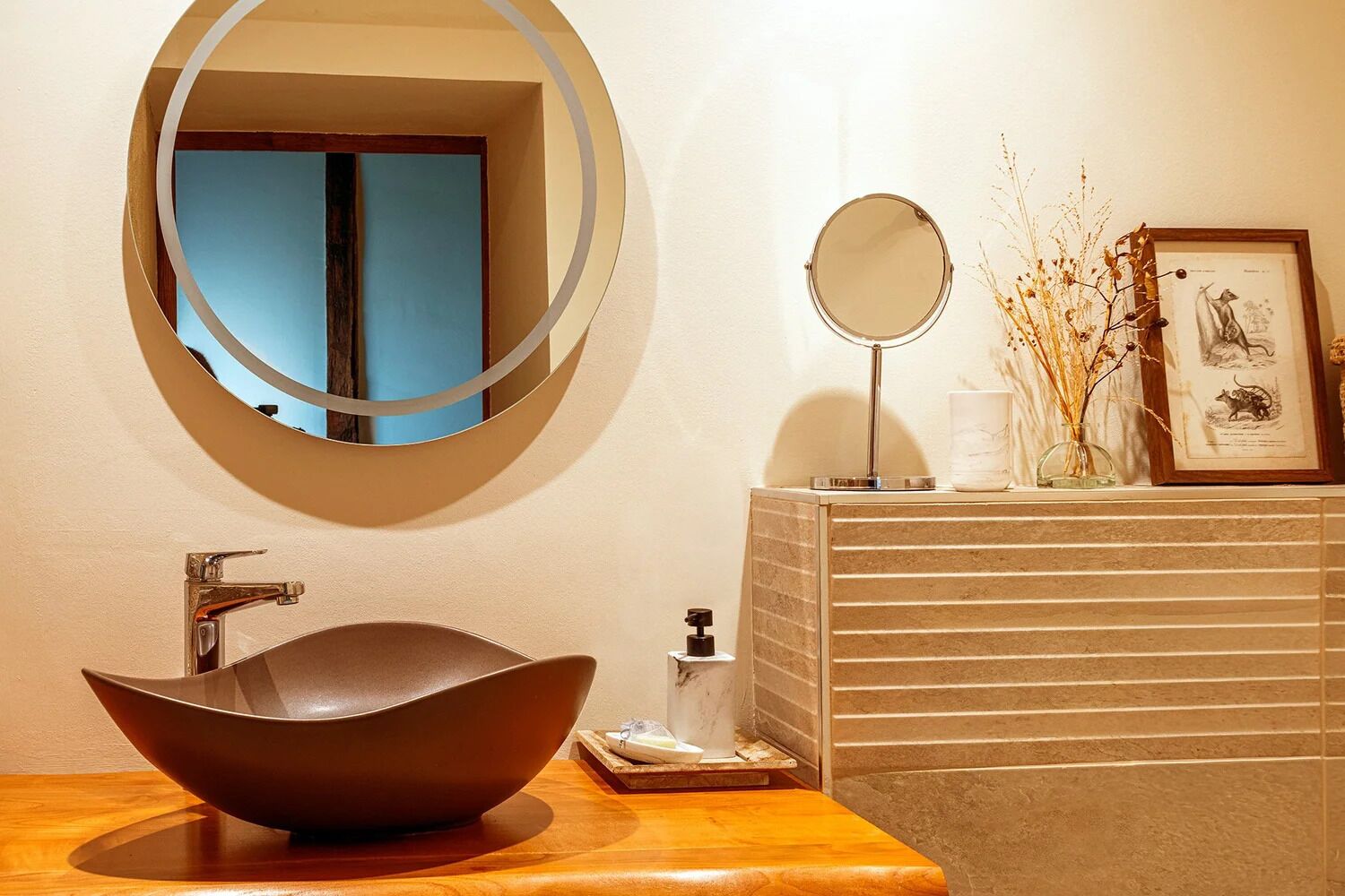A bathroom with a round mirror, a vessel sink, and a framed picture on the wall.
