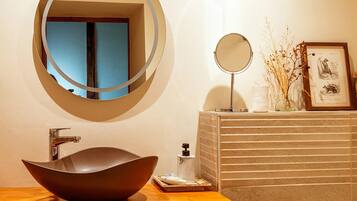 A bathroom with a round mirror, a vessel sink, and a framed picture on the wall.