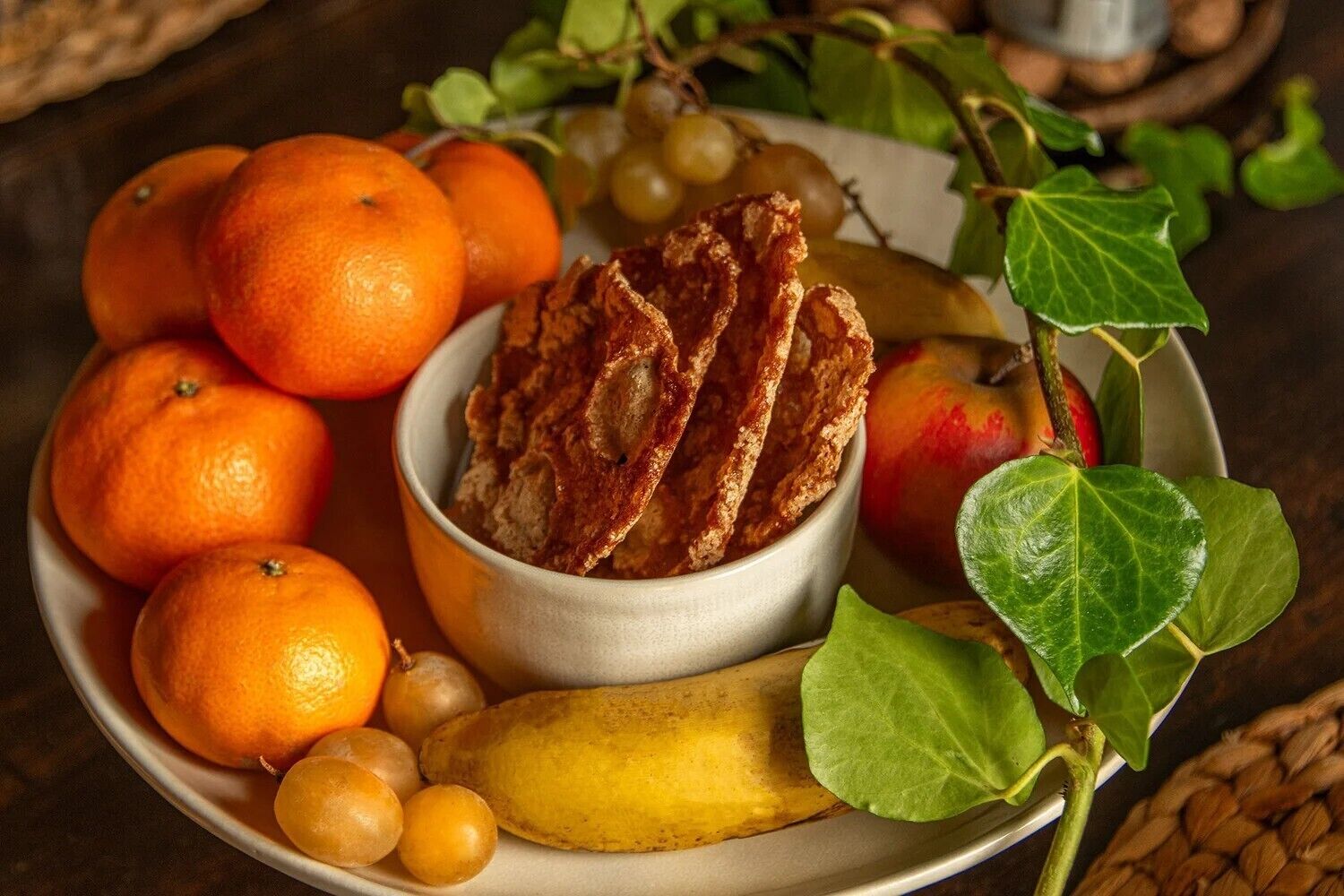 Une assiette contenant des oranges, des raisins, une banane et un bol qui semble contenir des fruits secs ou des noix.