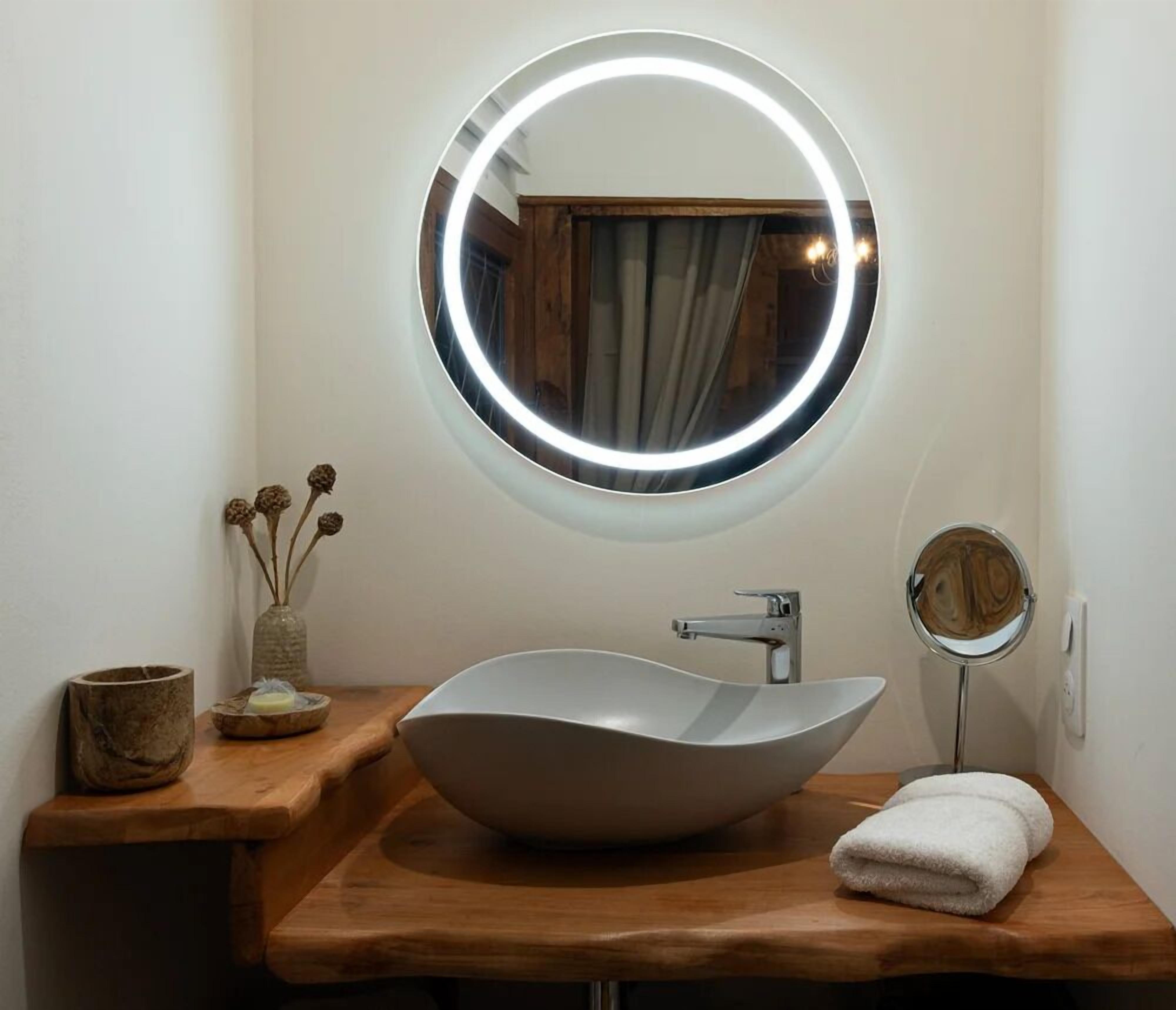 A bathroom with a round mirror, a vessel sink, a towel, and a small vase with dried flowers.