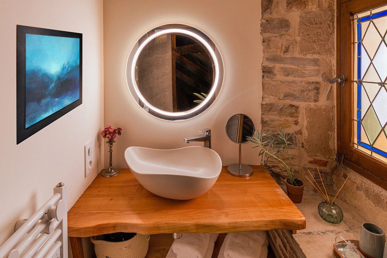 Une salle de bain avec une baignoire sur pieds, un miroir rond, une œuvre d’art encadrée et une plante en pot.