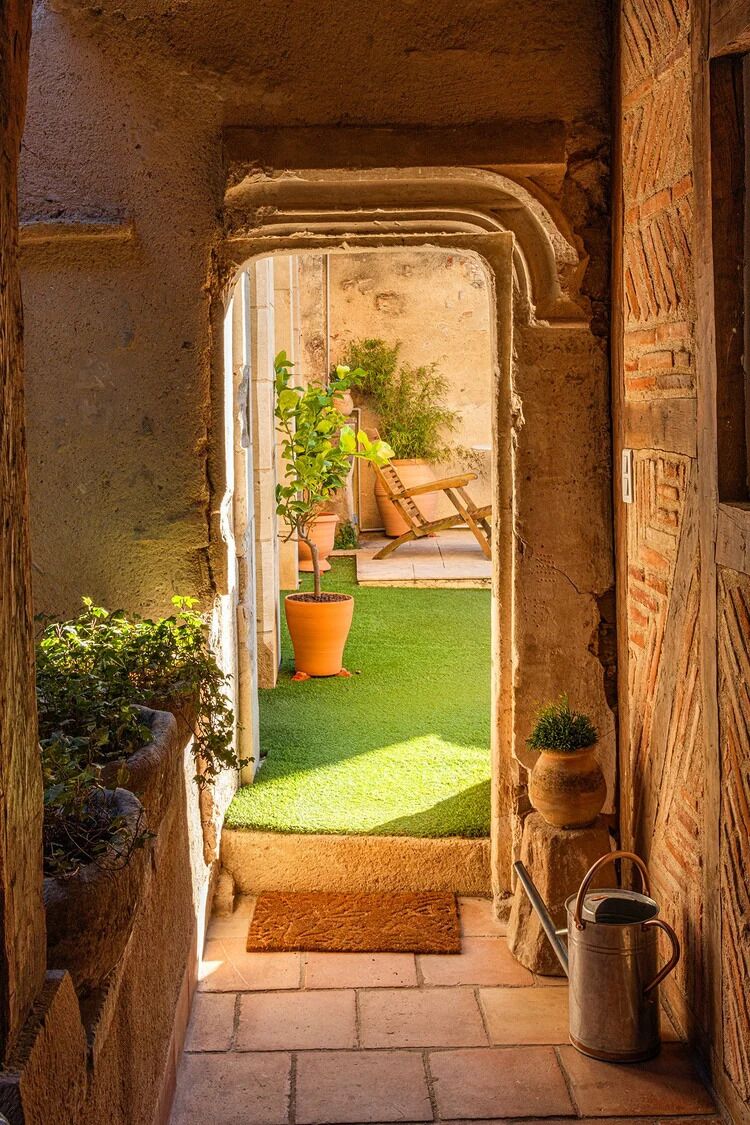 Un arc d'entrada que condueix a un pati amb gespa, plantes en testos i un regador de metall.