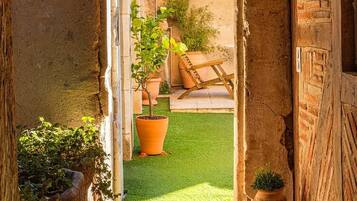 Un arc d'entrada que condueix a un pati amb gespa, plantes en testos i un regador de metall.