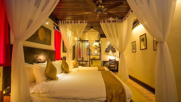 Una habitación de hotel con cama, cortinas, ventilador de techo y una mesita con lámpara.