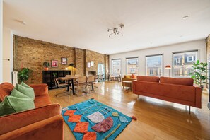 Un salon spacieux avec un mur en briques, un plancher en bois et une grande fenêtre.