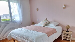 A bedroom with a wooden floor, a bed with white bedding, a pink wall, and a window with curtains. - Regnéville sur Mer, gîte de La Sienne, between sea and countryside. (Regnéville-sur-Mer)