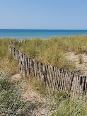 A sandy beach with a wooden fence and tall grass. - Regnéville-sur-Mer, La Sienne Vacation Home, between the sea and the countryside. (Regnéville-sur-Mer)