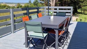 An outdoor deck with a table and chairs, a large umbrella, and a view of the landscape. - Regnéville sur Mer, gîte de La Sienne, between sea and countryside. (Regnéville-sur-Mer)