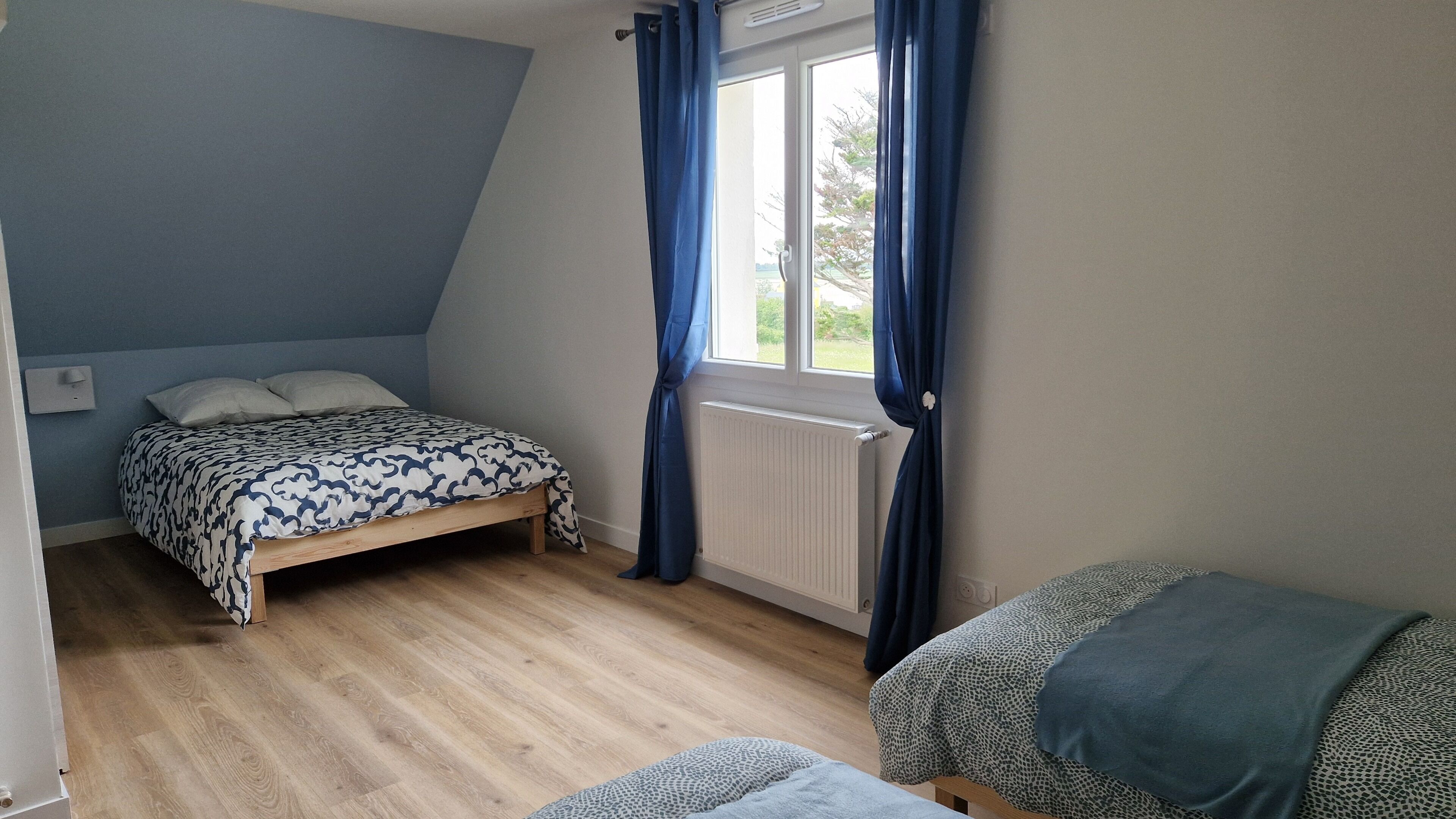 A bedroom with a bed, a window with curtains, a radiator, and a small table.