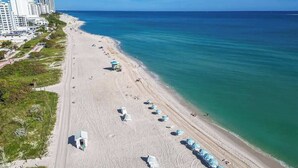 A beach with rows of umbrellas and a few buildings in the background. - Oceanfront 2BR at The Alexander · Pools + Beach (Miami)
