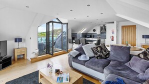 A modern loft-style living space with a large sliding glass door leading to a balcony, a cozy seating area with a sofa, a coffee table, and a TV. - Beachfront apartment in Rock - Parking - Sea Views (Rock)