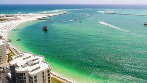 An aerial view of a coastal area with a beach, a pier, and a boat in the water. - 3BR Harbor front + Panoramic Views + Pool & Beach Access | East Pass Towers (Destin)