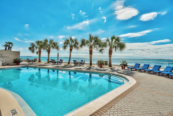 A pool area with clear blue water, palm trees, and a view of the ocean.