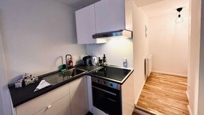 A compact kitchen with a black countertop, white cabinets, a built-in oven, and a geometric pendant light. - Central charming apartment in the old town center (Bayreuth)