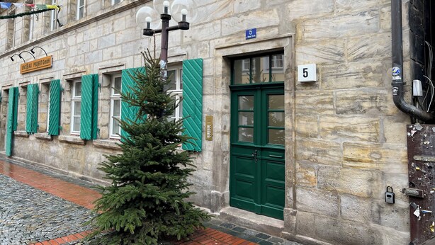 A stone building with a green door and windows, a Christmas tree, and a sign reading "UNIT B AU PROJEKT GmbH". - Central charming apartment in the old town center (Bayreuth)