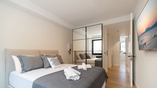 Une chambre d’hôtel moderne avec un grand lit, un miroir et un tableau représentant un coucher de soleil.