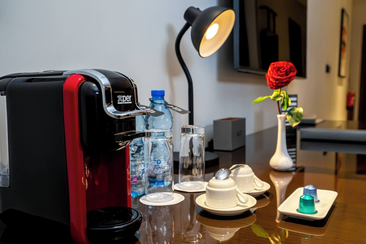 Una cafetera, botellas de agua, una rosa en un florero y una lámpara de escritorio en una habitación de hotel.