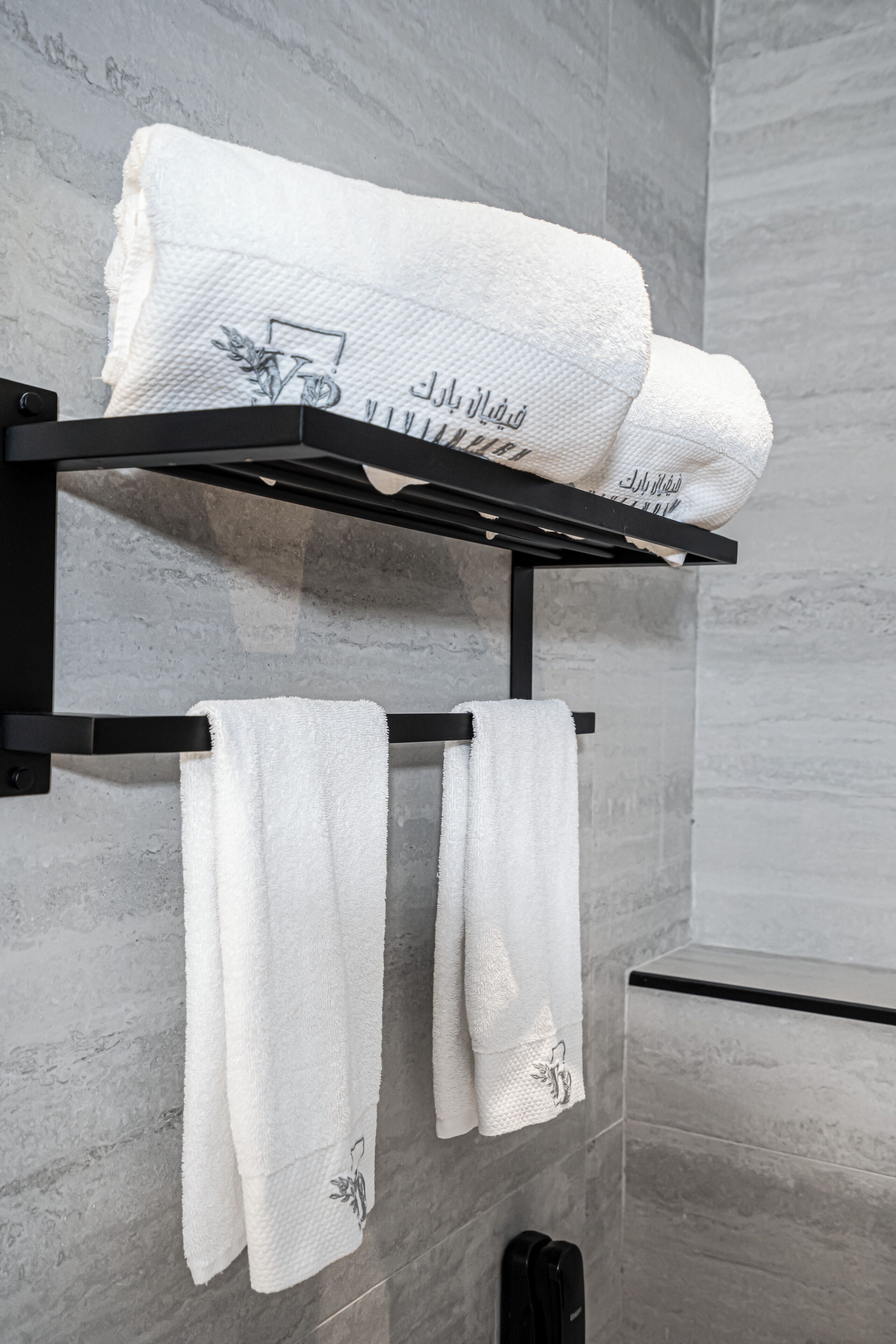 A bathroom with a towel rack holding two white towels and a folded towel with a floral design.