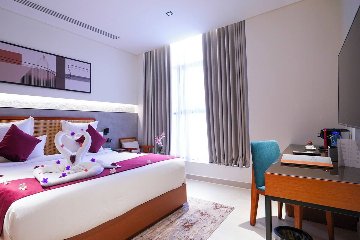 Una habitación de hotel con una cama grande, un escritorio, una silla, un televisor y una ventana con cortinas.