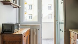 Una pequeña cocina con alacenas de madera, un microondas, un refrigerador y una ventana con vista a un edificio.